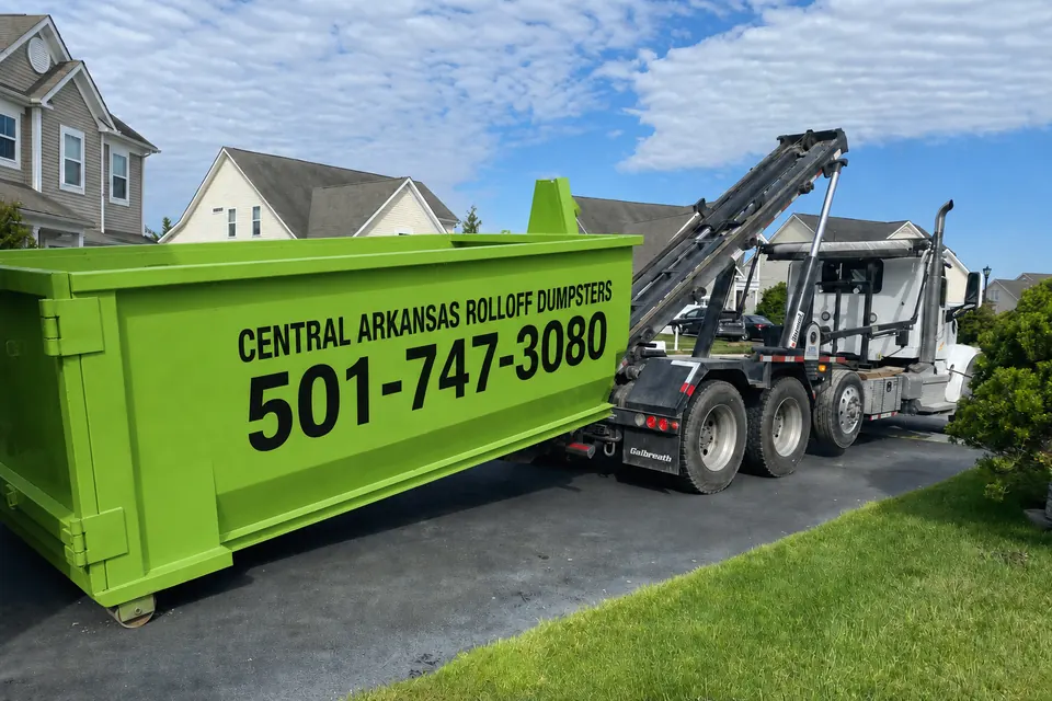 Central Arkansas Rolloff Dumpsters truck delivering a green roll-off dumpster to a residential property